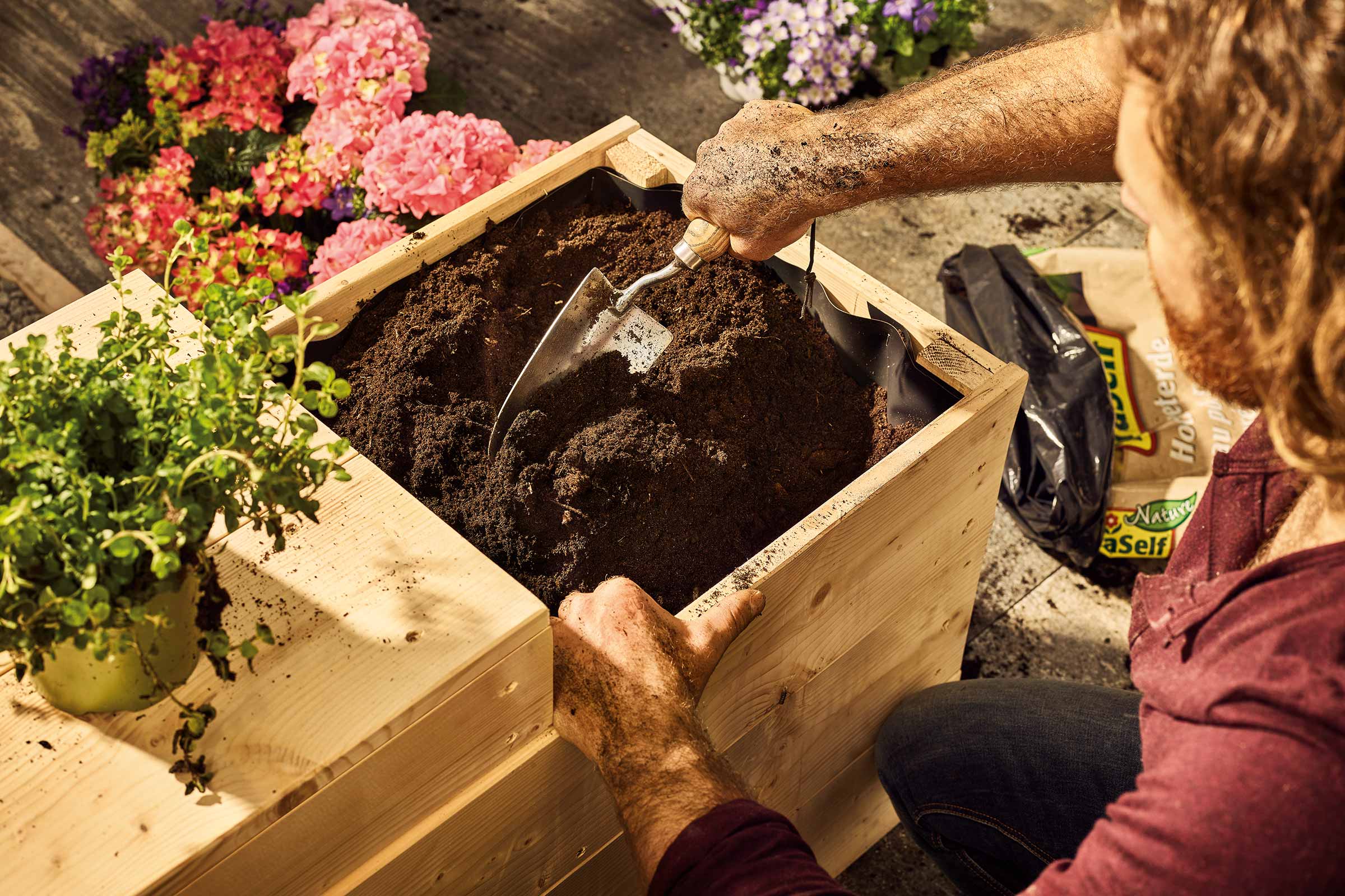 Een persoon vult een houten plantenbak met aarde met behulp van een kleine schep.