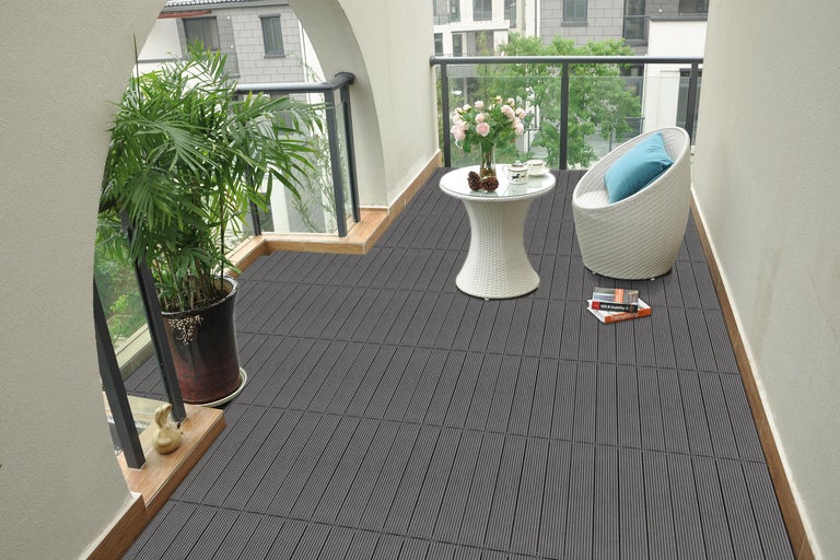 Balkon met grijze terrasplanken, tafel, stoel en potplant.