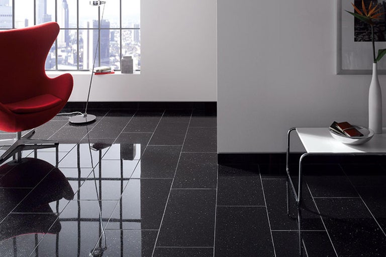 Interieur met donkere vloertegels, gecombineerd met een rode fauteuil en een kleine bijzettafel.