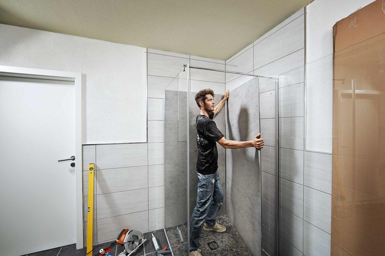 Een man installeert een douchecabine in een betegelde badkamer.
