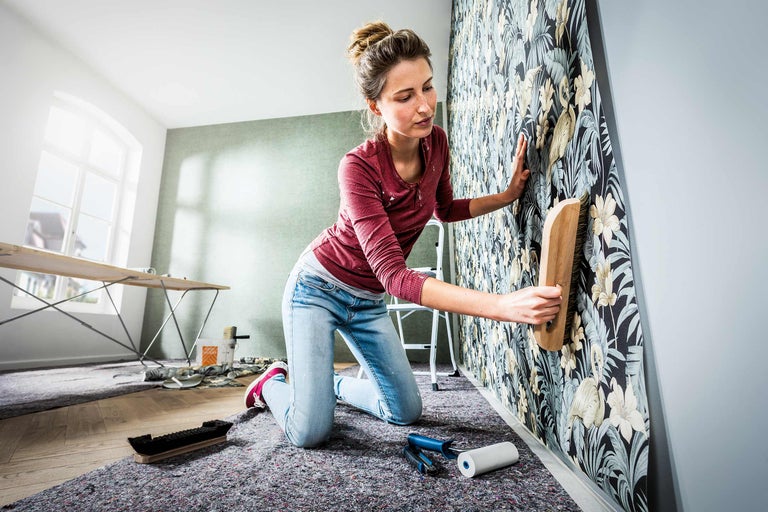 Vrouw behangt een muur met een borstel, met bloemenpatroon in een kamer.