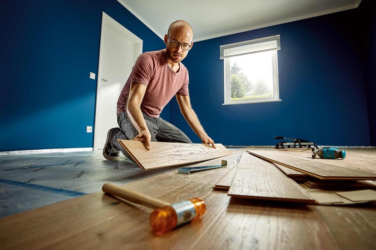 Man legt laminaatvloer in een kamer met gereedschap.