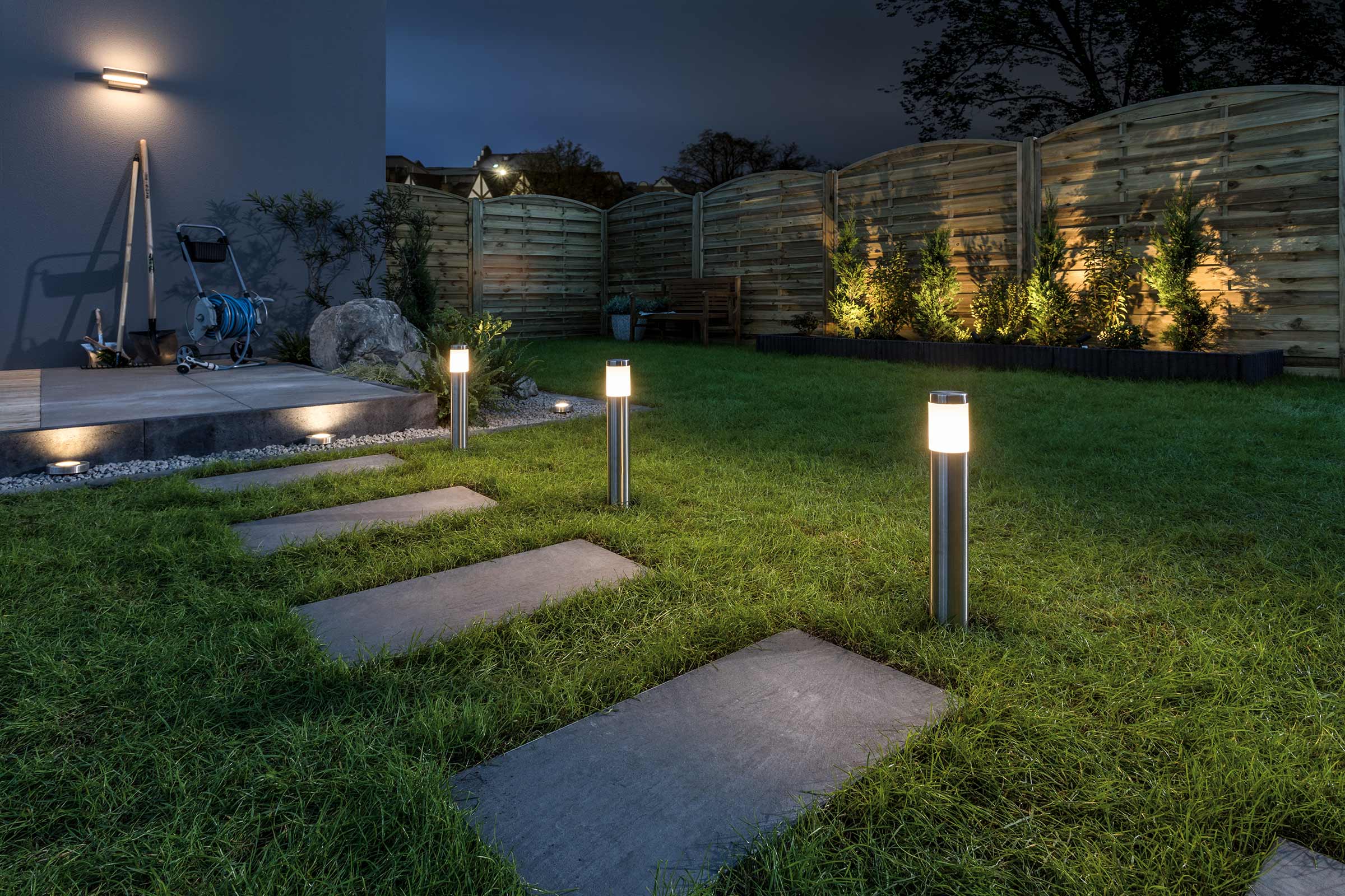 Verlichte tuin met gazon, looptegels en tuinafscheiding
