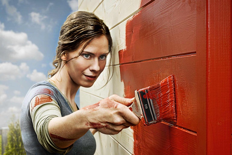 Vrouw schildert houten gevel met een kwast en houtverf