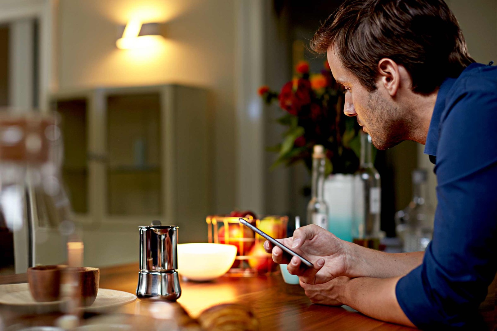 Man kijkt naar een mobiele telefoon aan een tafel met een espressopot en servies.