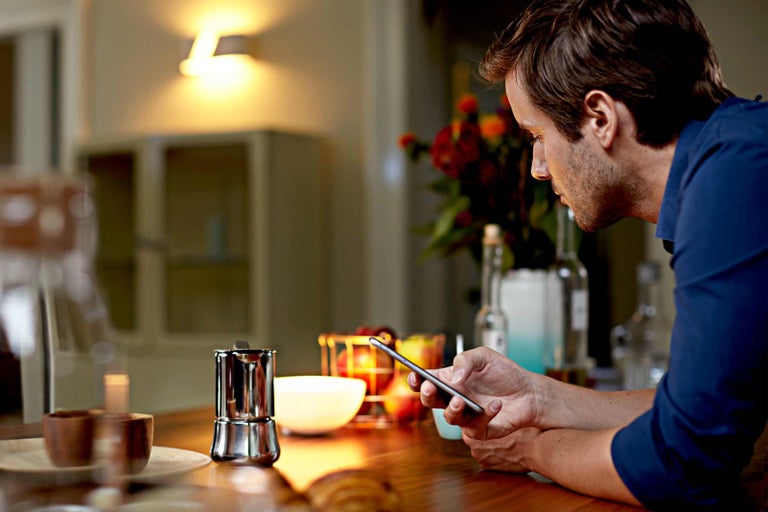 Man kijkt naar een mobiele telefoon aan een tafel met een espressopot en servies.