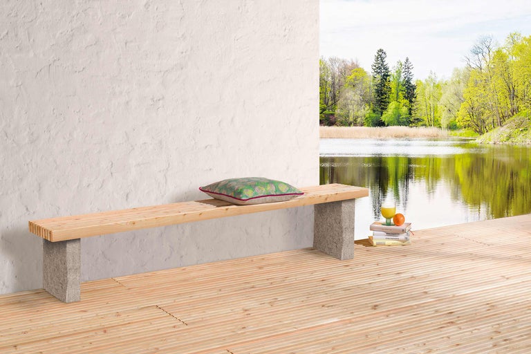 Houten bank met stenen poten, kussen, drankje en boeken op een houten terras met uitzicht op het meer