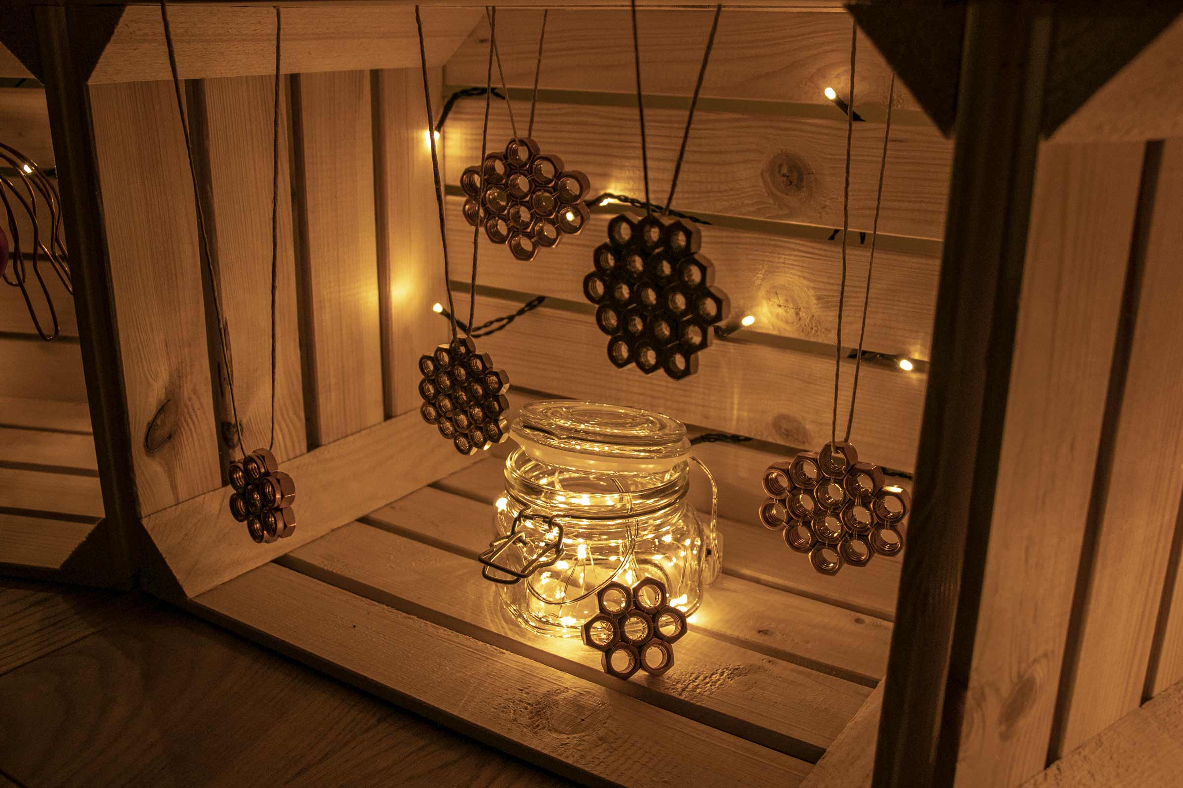 Decoratieve scène met een jampot met lichtjes en hangers van moeren in een houten kist.