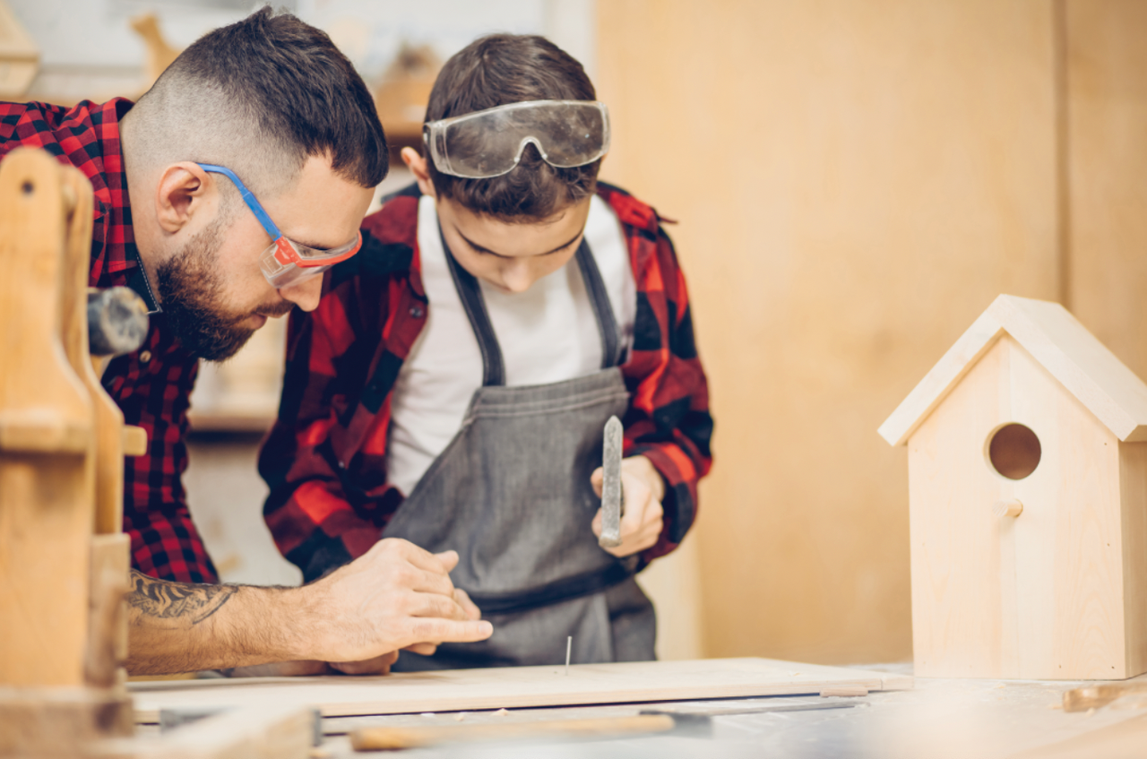 Vader en zoon bouwen samen een vogelhuis met hamer en spijker.