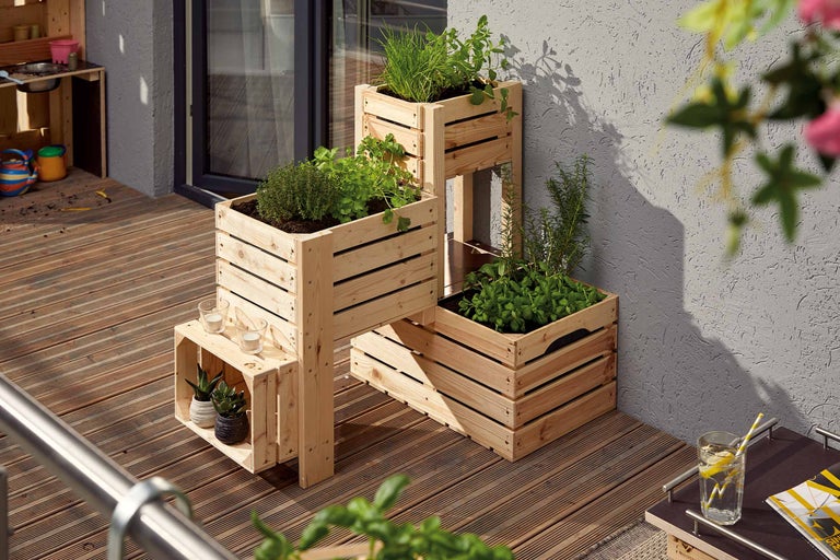Gelaagde kruidentuin gemaakt van houten kisten op een balkon met houten vloer.
