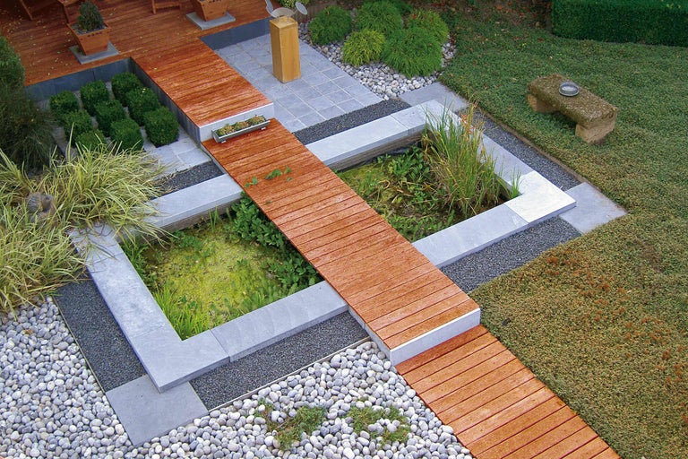 Overzicht van een tuinvijver met houten loopbrug, omgeven door stenen en planten