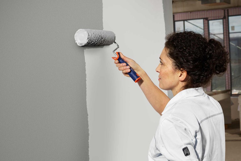 Vrouw schildert muur grijs met verfroller