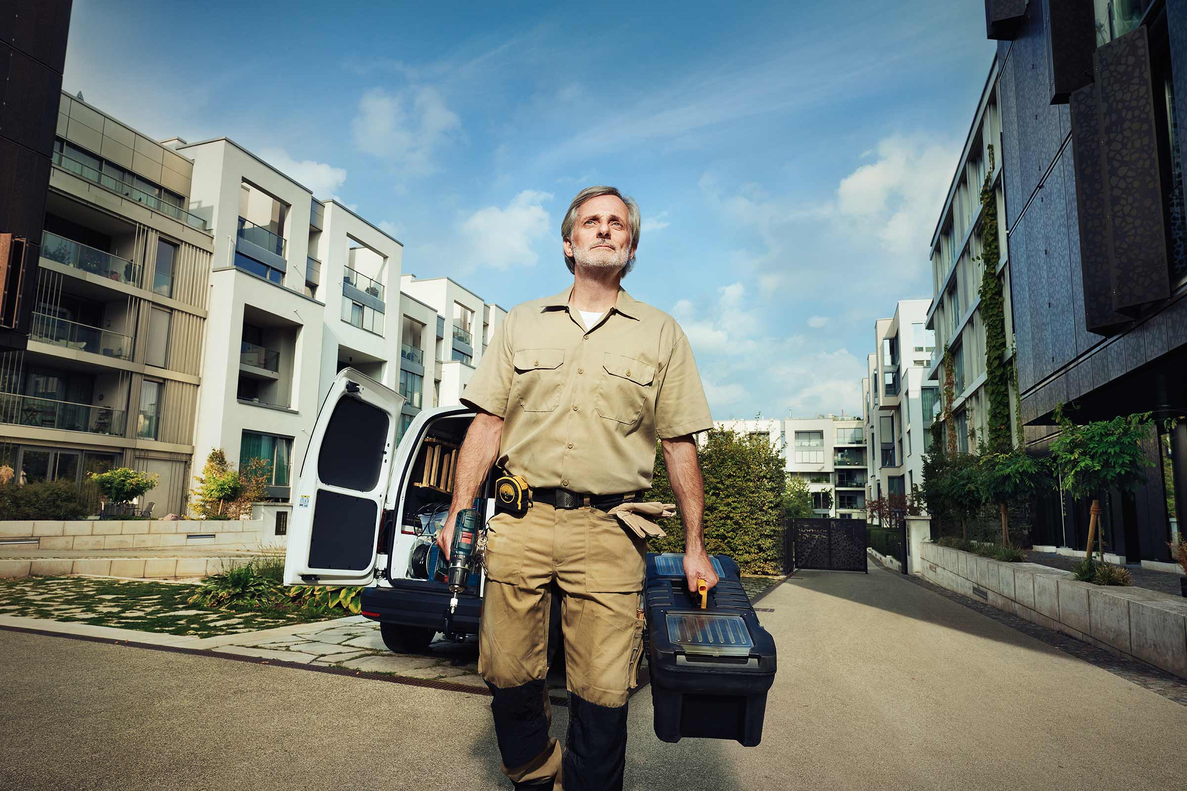 Vakman met gereedschapskist en boormachine voor een bestelwagen en woongebouwen