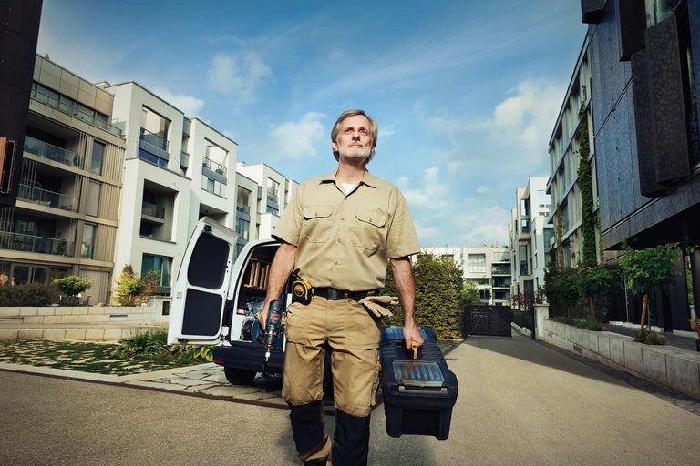 Vakman met gereedschapskist en boormachine voor een bestelwagen en woongebouwen