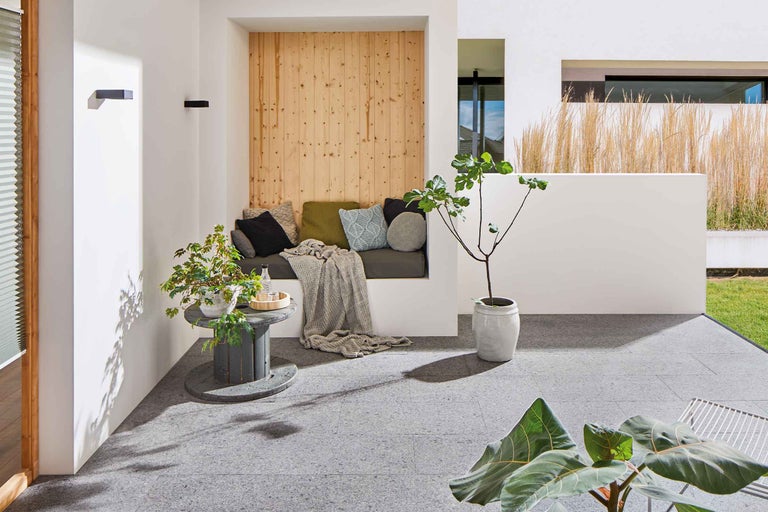 Modern ontworpen buitenruimte met zithoek, planten en vloerplaten.