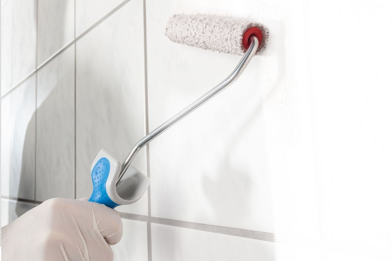 Een persoon met handschoenen gebruikt een verfroller om een muur te schilderen.