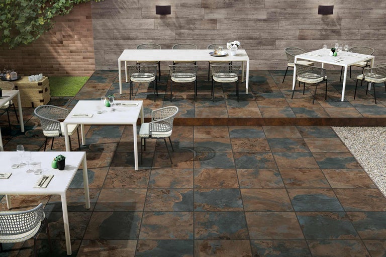 Terras met vloertegels, tafels en stoelen in de buitenruimte.