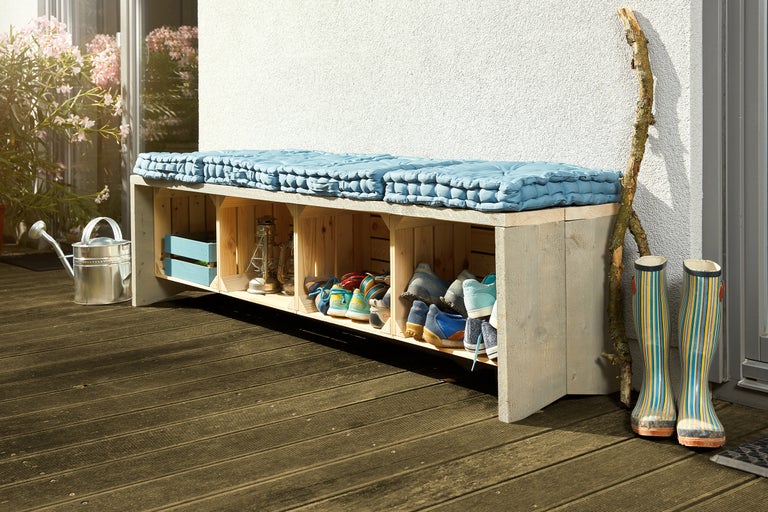 Garderobebank van houten kisten met schoenenrek en zitkussen op een terras met gieter en laarzen
