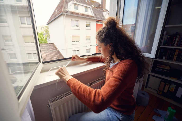 Vrouw bevestigt afdichtband aan een raamkozijn voor raamafdichting