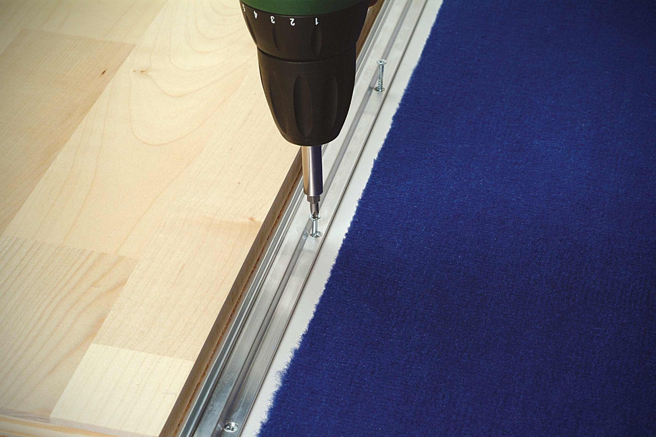 Montage van een tapijtstrip met een accuschroevendraaier op een houten vloer