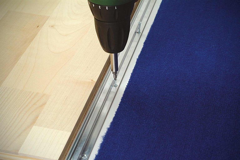 Montage van een tapijtstrip met een accuschroevendraaier op een houten vloer