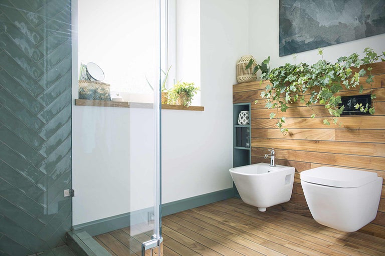 Moderne badkamer met douche, bidet en toilet tegen een houten wand met planten
