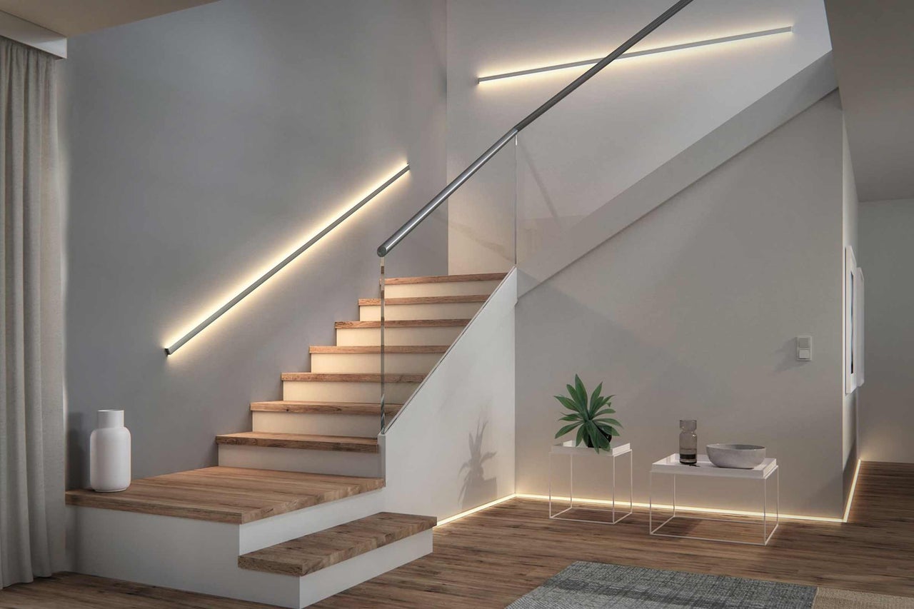 Trappenhuis met houten treden, glazen balustrade en lineaire wandlampen