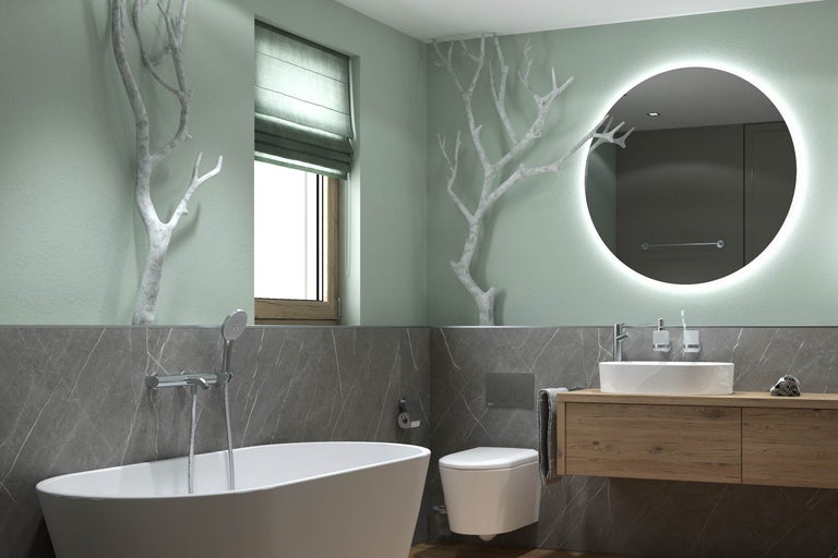 Moderne badkamer met vrijstaand bad, hangend toilet en houten wastafelmeubel. Grote ronde spiegel met verlichting en decoratieve takken aan de wand.