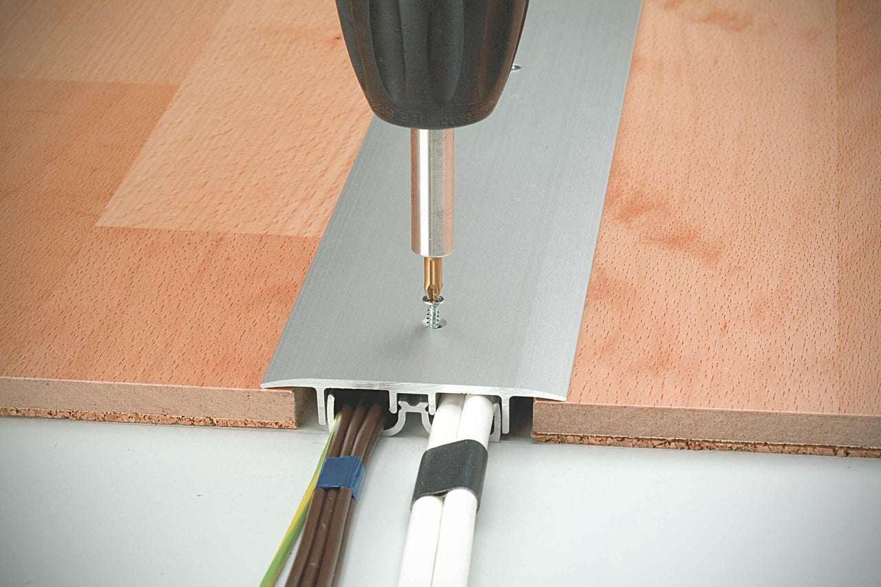 Bevestiging van een aluminium kabelbeschermingsstrip op een houten vloer met een schroevendraaier