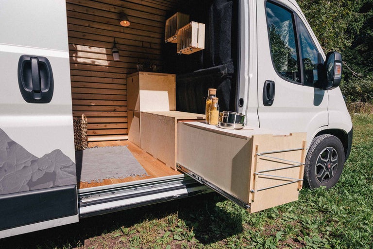 Interieur van een campervan met houten bekleding, uitschuifbare keuken en proviand