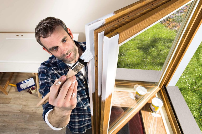 Man schildert met een kwast een houten raamkozijn met lak.