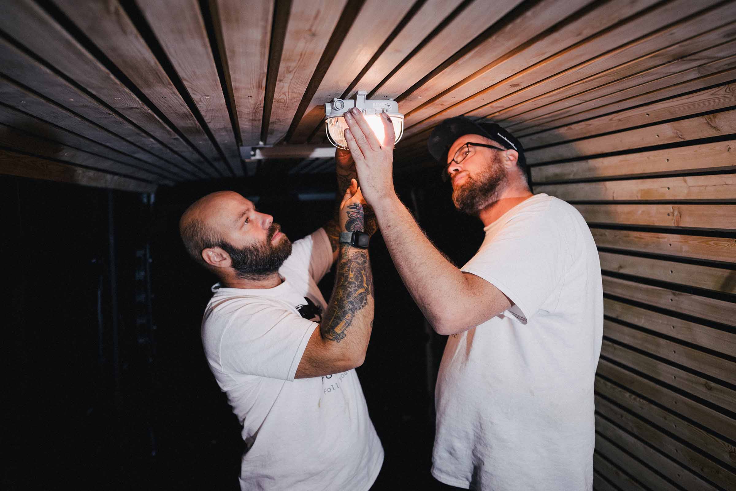 Twee mannen installeren een lamp aan een houten plafond.