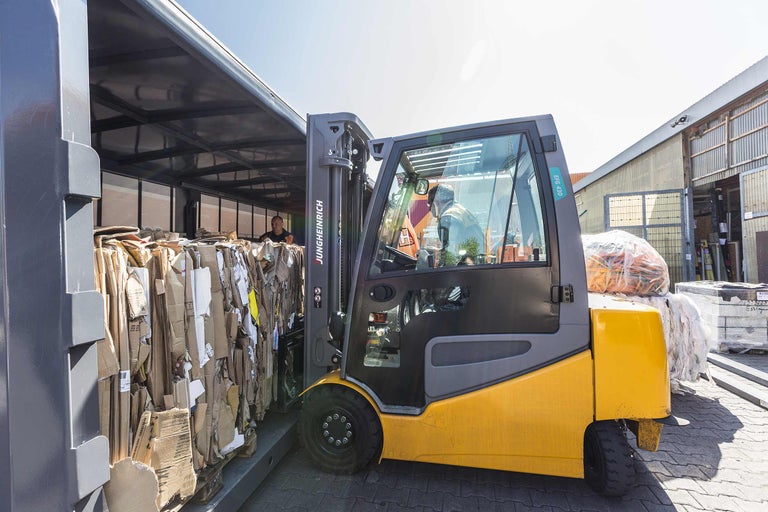 Heftruck bij het lossen van oud papier in een container