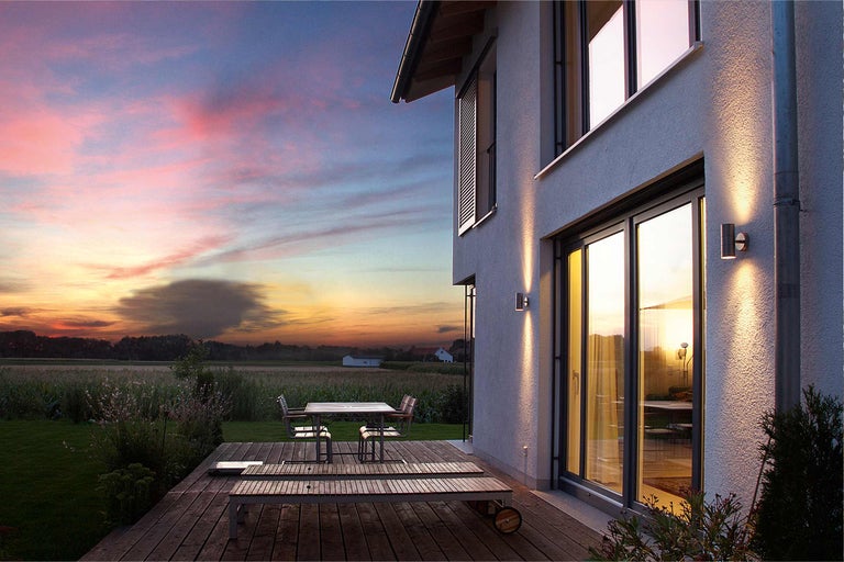 Buitenaanzicht van een modern huis met terras en tuinmeubelen bij zonsondergang