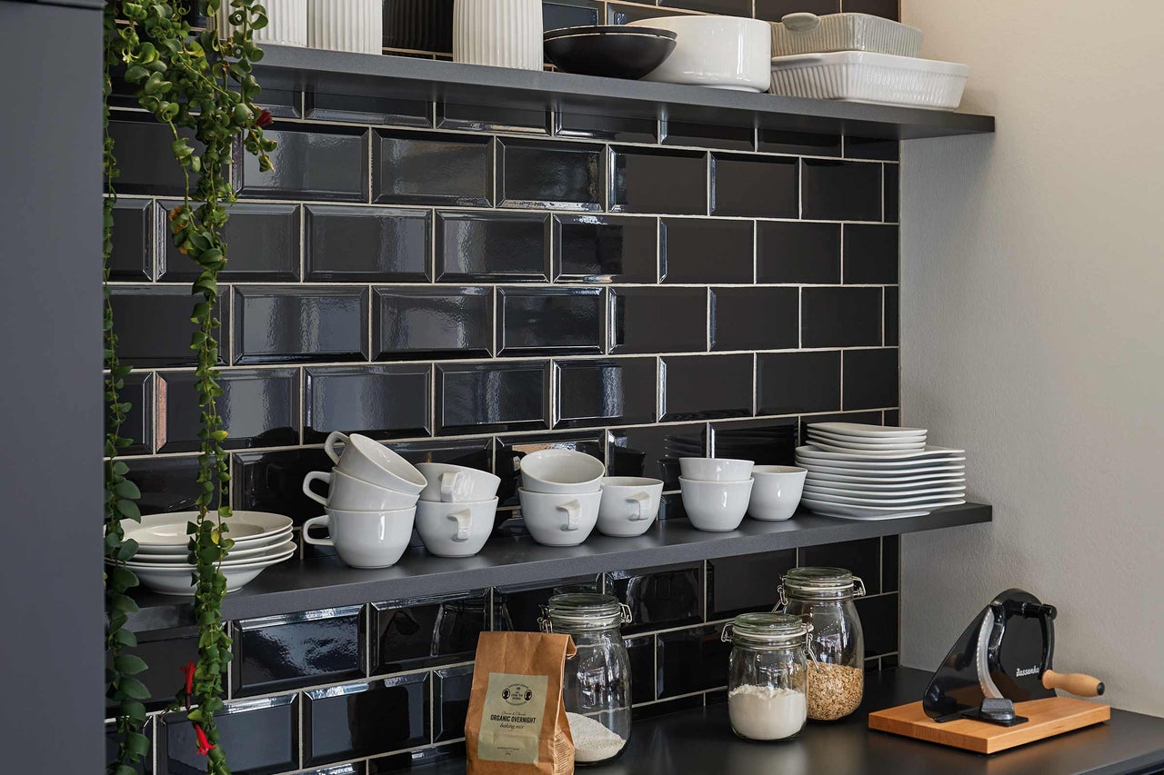 Planken met servies en zwarte tegels in de keuken