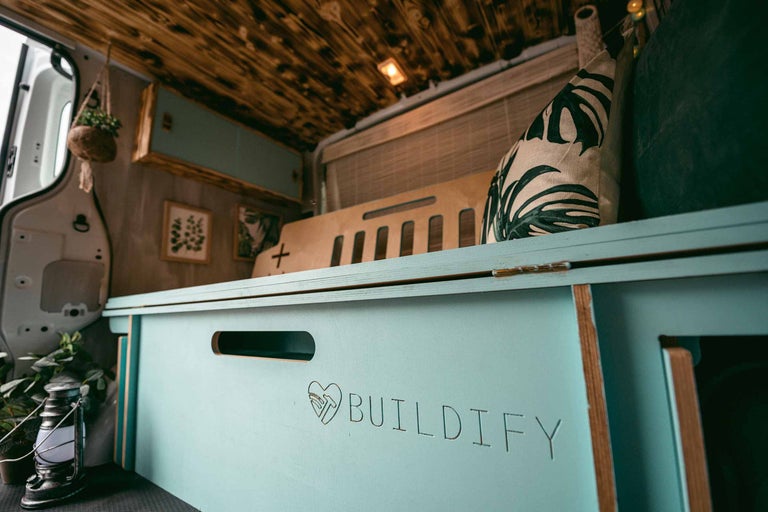 Interieur van een omgebouwde bestelwagen met houten plafond, mintkleurige kasten, decoratieve kussens en het opschrift Buildify