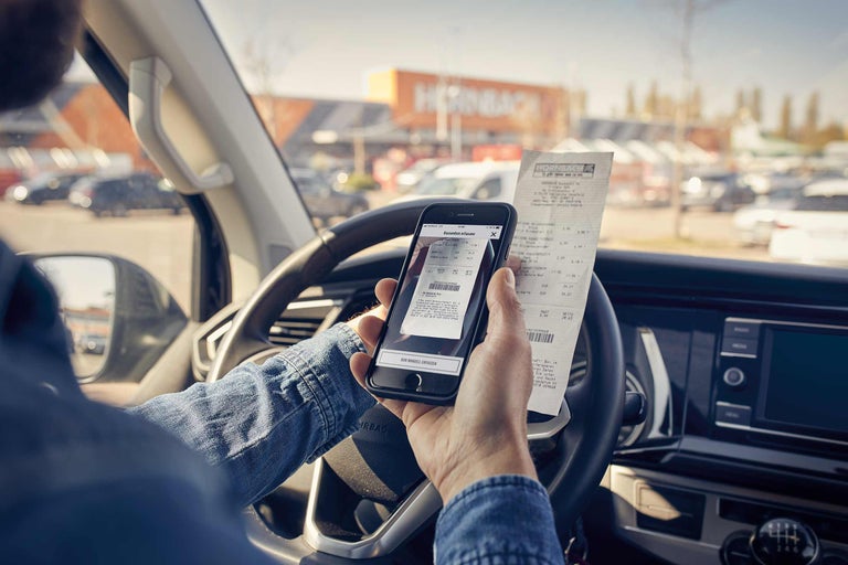 Iemand zit in de auto en fotografeert een Hornbach-kassabon met een smartphone.