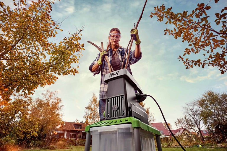 Vrouw gebruikt een tuinhakselaar om takken in de tuin te versnipperen.