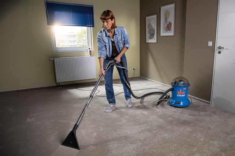 Vrouw reinigt tapijt met een tapijtreinigingsapparaat in een kamer.