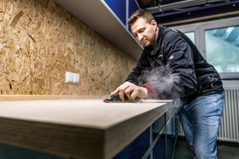 Een man schuurt een houten oppervlak in een werkplaats.