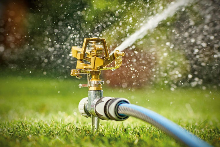 Metalen cirkelsproeier met tuinslang in gebruik op gazon