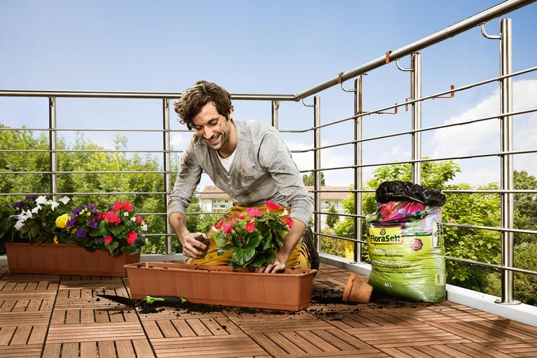 Man plant bloemen op een balkon met potgrond in een bloembak.