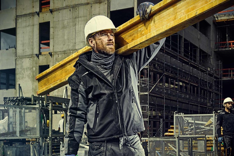 Bouwvakker met veiligheidshelm draagt houten balk op een bouwplaats