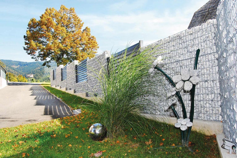 Schanskorfomheining met siergras en metalen bol in de tuin