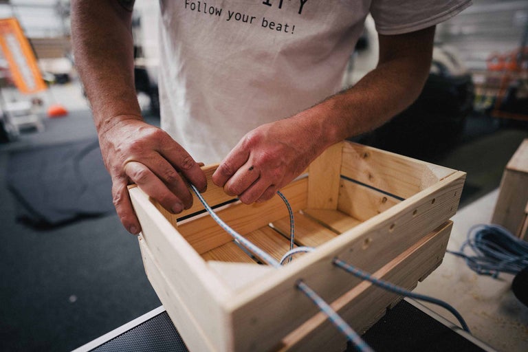 Man rijgt een elastisch koord in een houten kist