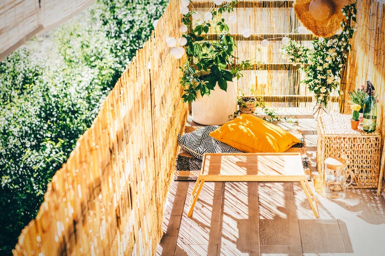 Balkon met bamboe schutting, planten, kussens, tafel en gevlochten kruk