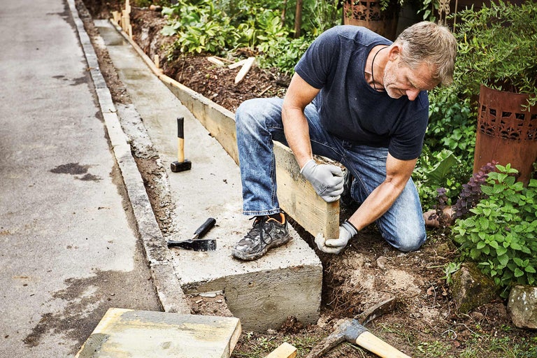 Een man werkt aan een betonnen gazonrand met houten bekisting in een tuin.