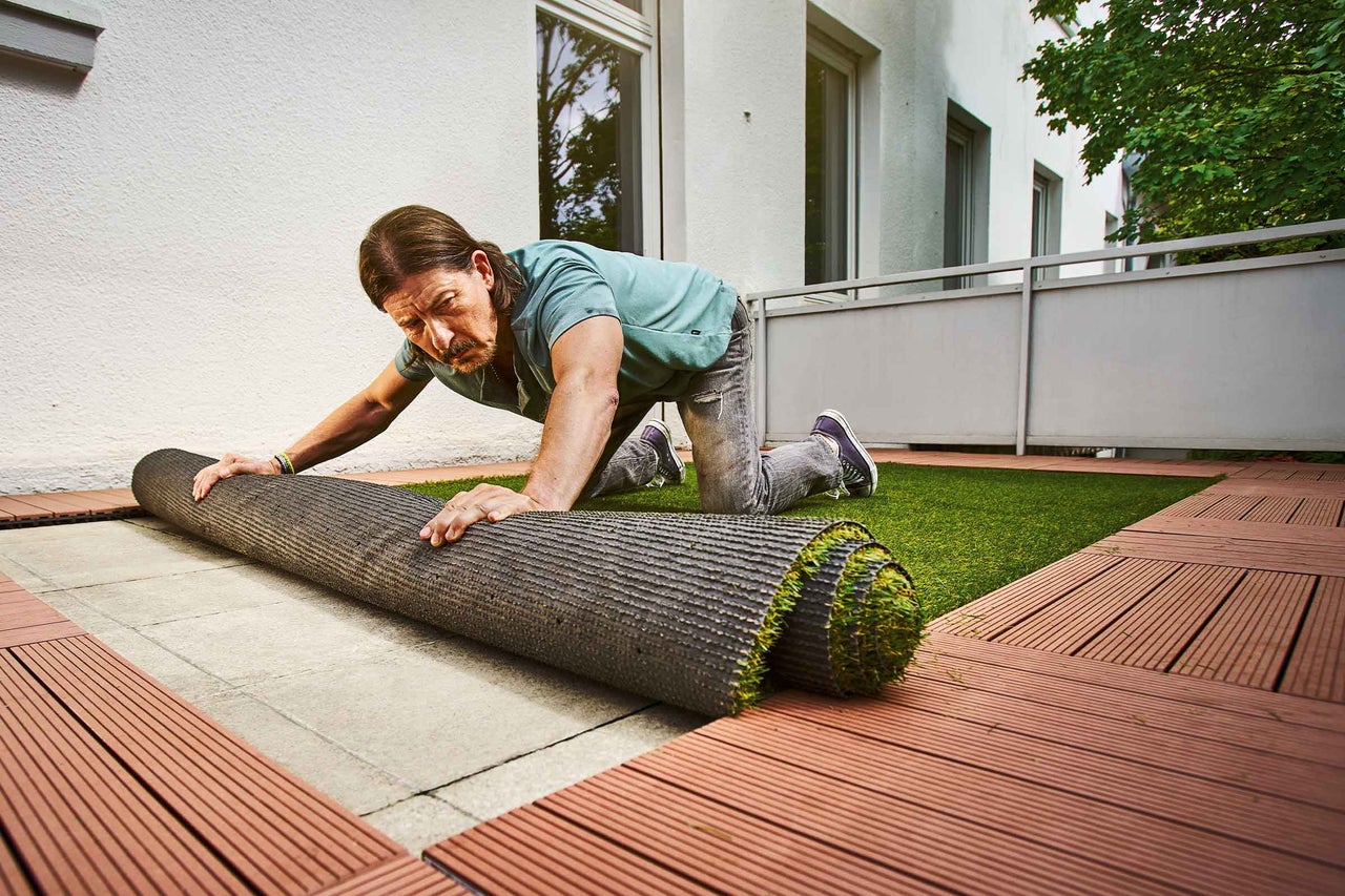 Iemand rolt kunstgras uit op een balkon dat is belegd met terrasplanken.