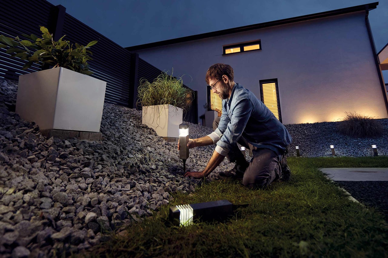 Een man installeert tuinverlichting in een tuin met grind en planten