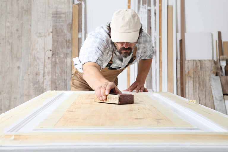 Man schuurt houten deur met schuurpapier